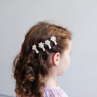 Child with floral hair clips in a side bun against a plain background