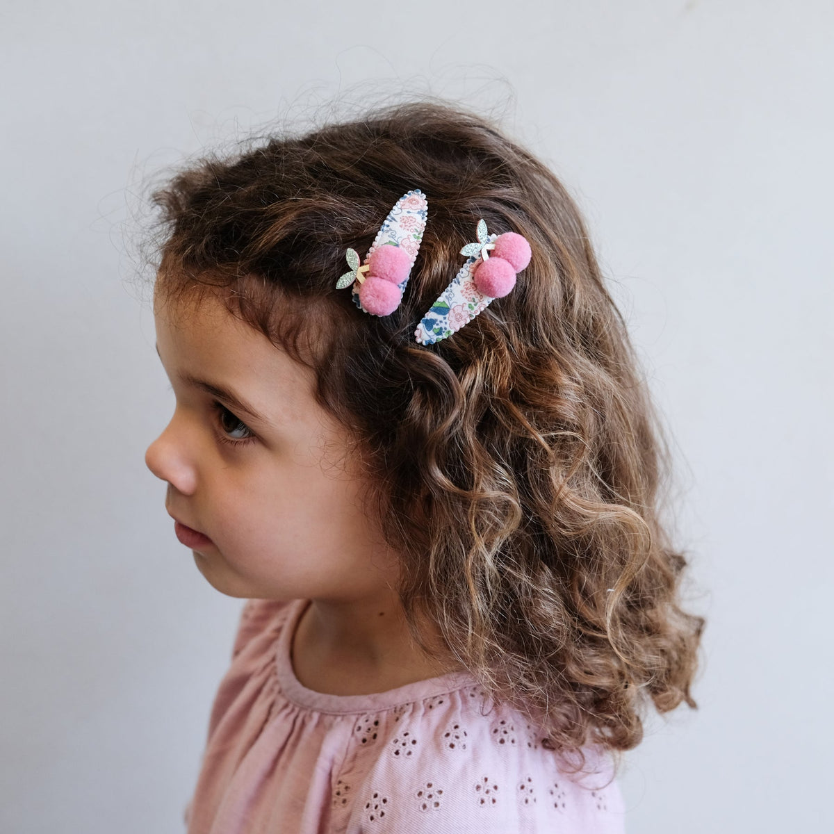 Child with floral hair clip and pink hair tie on a plain background