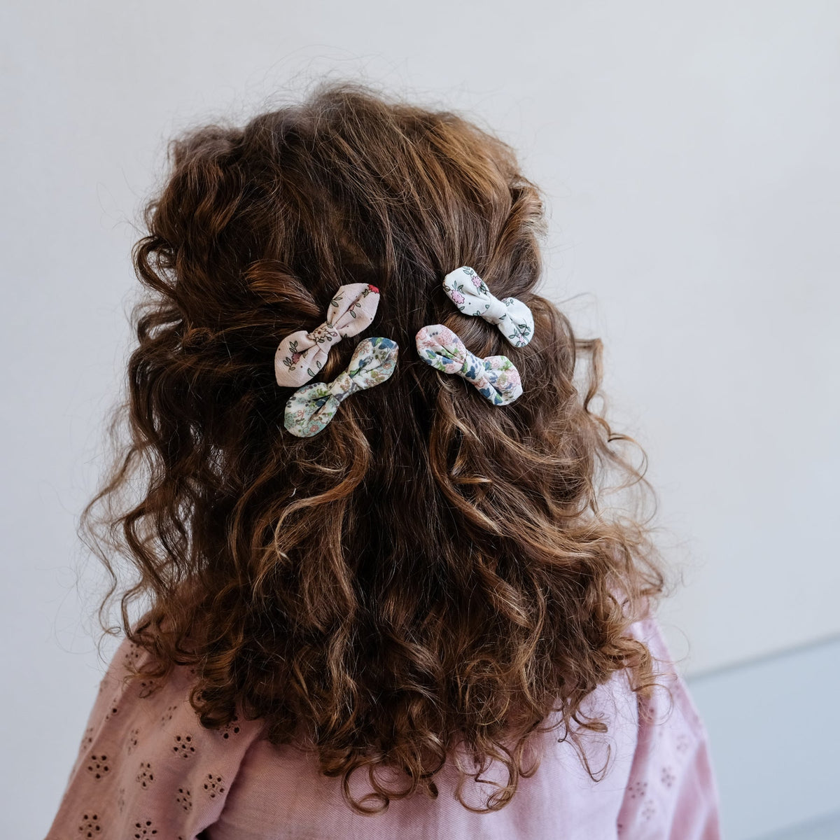 Person with curly hair wearing floral hair clips against a plain background
