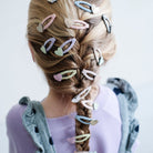 Person with braided hair adorned with colorful hair clips on a light background
