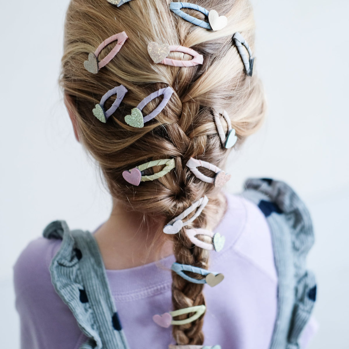 Person with braided hair adorned with colorful hair clips on a light background