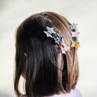 Person wearing colorful star-shaped hair clips on a plain background