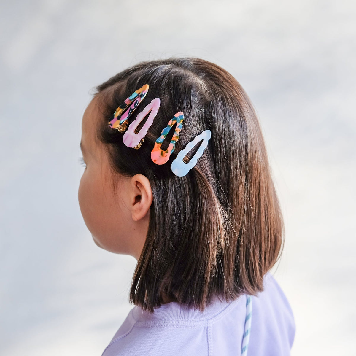 Child with colorful hair clips in their hair against a plain background