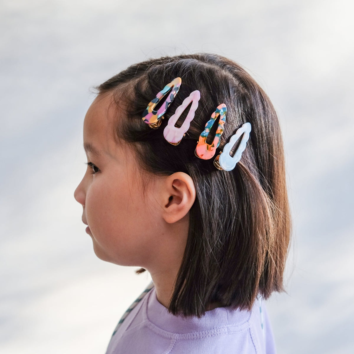 Child with colorful hair clips in their hair against a plain background