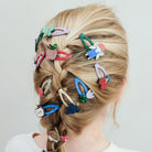 Person with braided hair adorned with colorful hair clips on a plain background