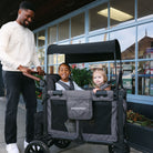 Man pushing a stroller with two children in front of a store.