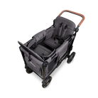 A high-angle studio shot of a stroller wagon attachment set against a solid white background. The stroller features a dark gray fabric body with a brown wooden handlebar and black wheels.