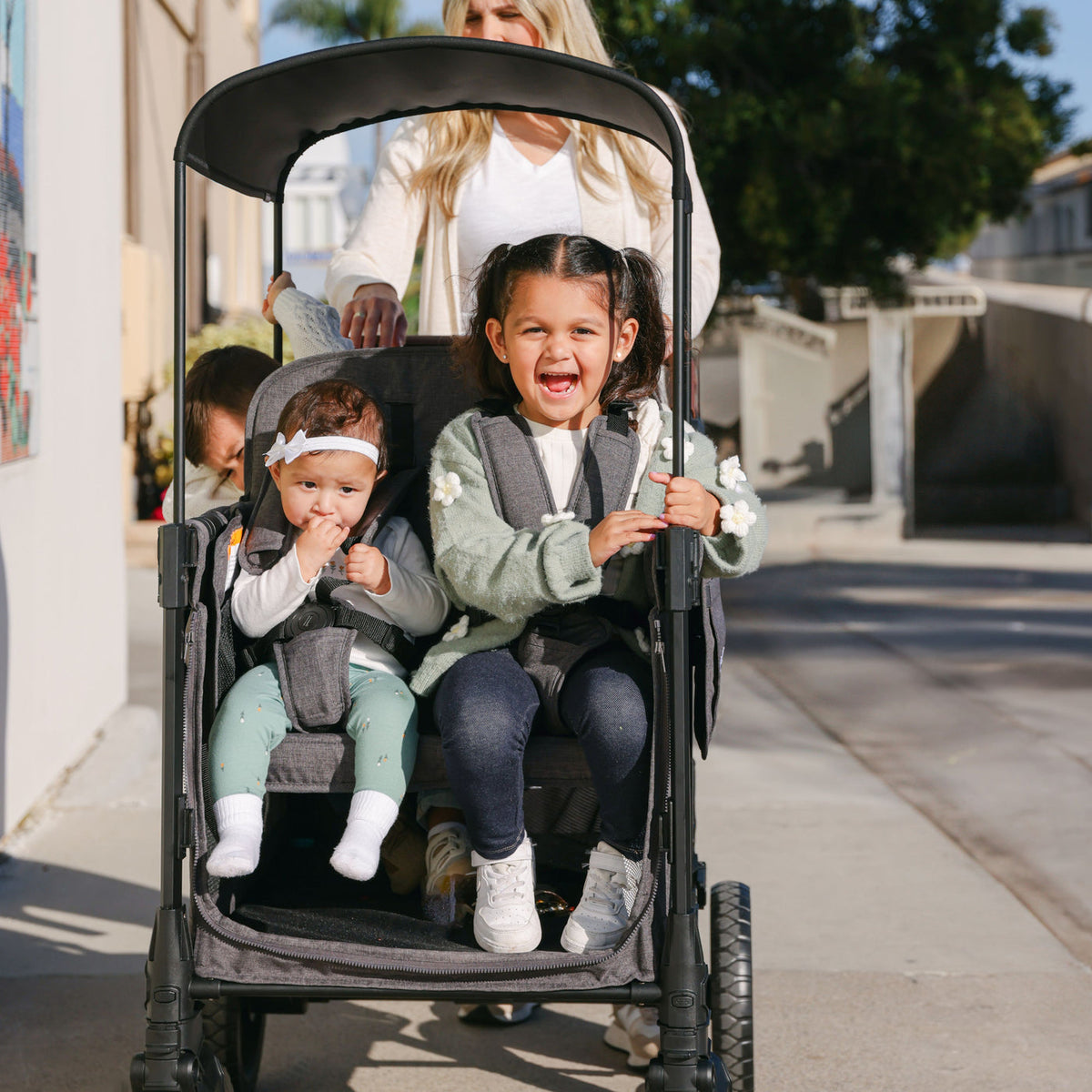 Three children in a stroller with a woman pushing them, outdoors.