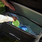 Person reaching into a black cooler with Wonderbag branding, filled with ice and colorful items.
