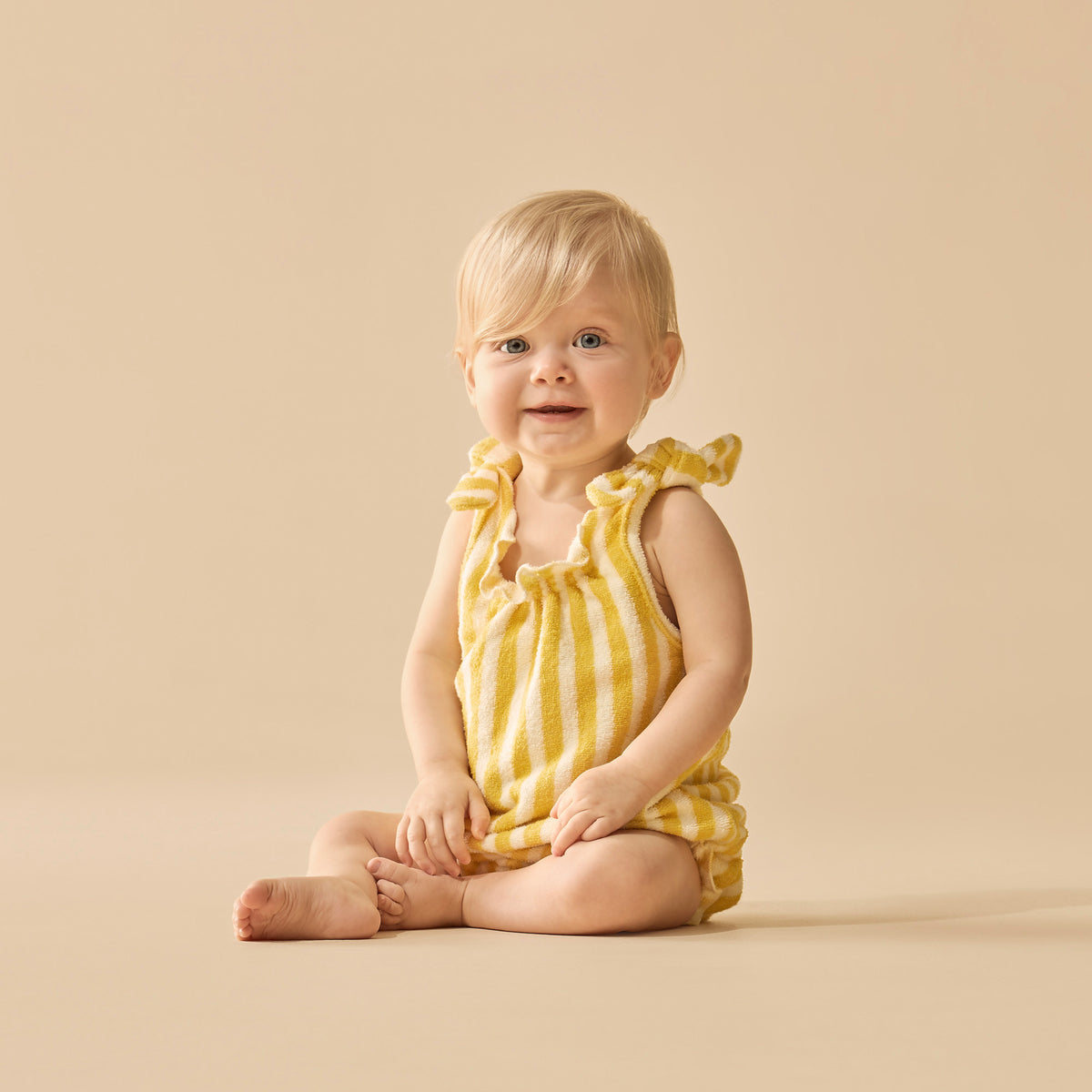 Baby wearing a yellow striped romper sitting on a beige background