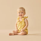 Baby wearing a yellow striped romper sitting on a beige background