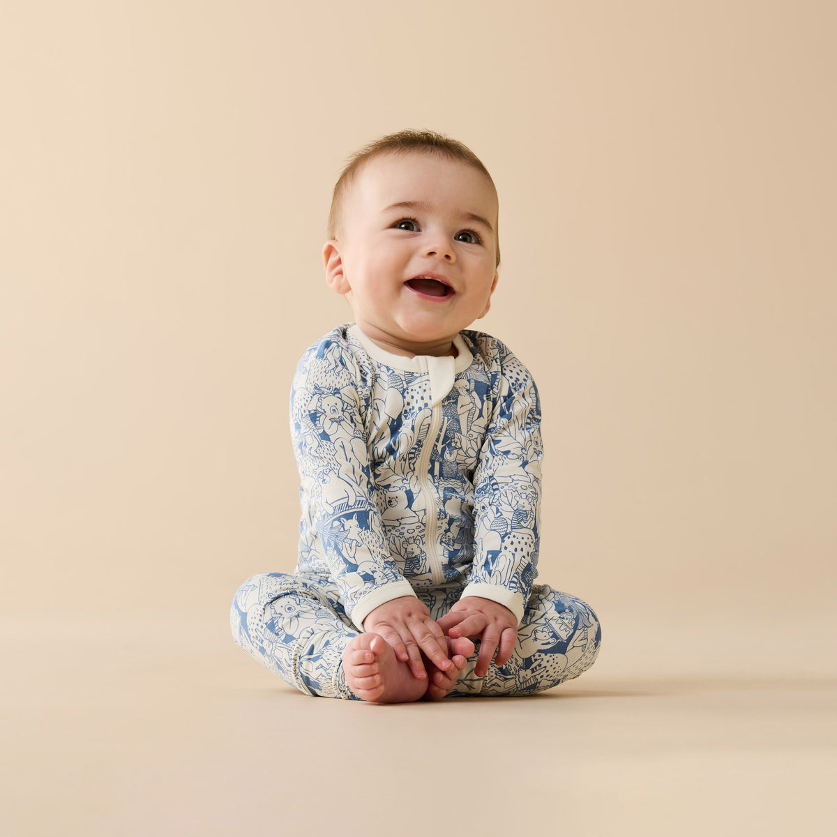 Baby wearing a patterned onesie sitting on a beige background