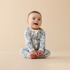 Baby wearing a patterned onesie sitting on a beige background