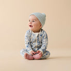 Baby wearing a patterned onesie and knitted hat sitting on a beige background