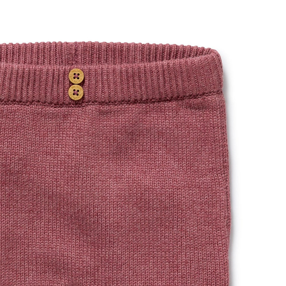 Close-up of a pink knitted garment with two buttons on a white background
