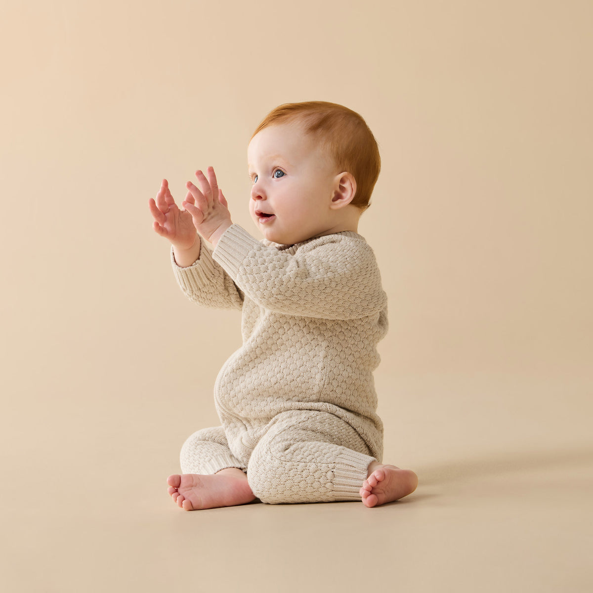 Baby in a cream knitted outfit sitting on a beige background