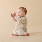 Baby in a cream knitted outfit sitting on a beige background