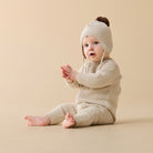 Baby wearing a beige knitted outfit and hat on a beige background