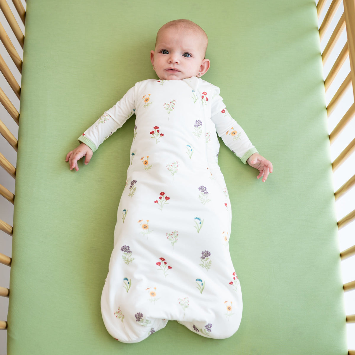 Baby lying in a crib with a floral-patterned white swaddle.