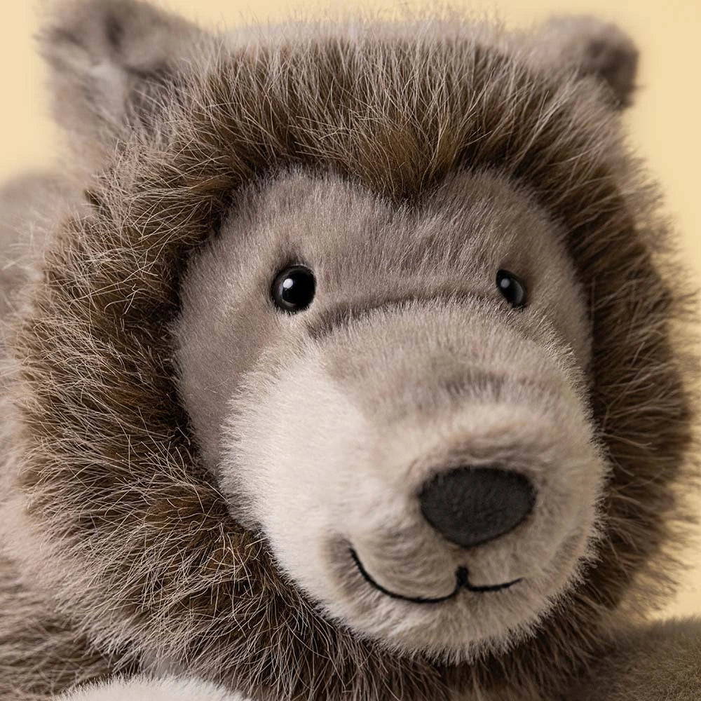 Close-up of a plush stuffed animal head with brown and gray fur, black eyes, and a stitched smile on a pale yellow background.
