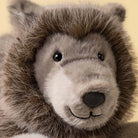 Close-up of a plush stuffed animal head with brown and gray fur, black eyes, and a stitched smile on a pale yellow background.