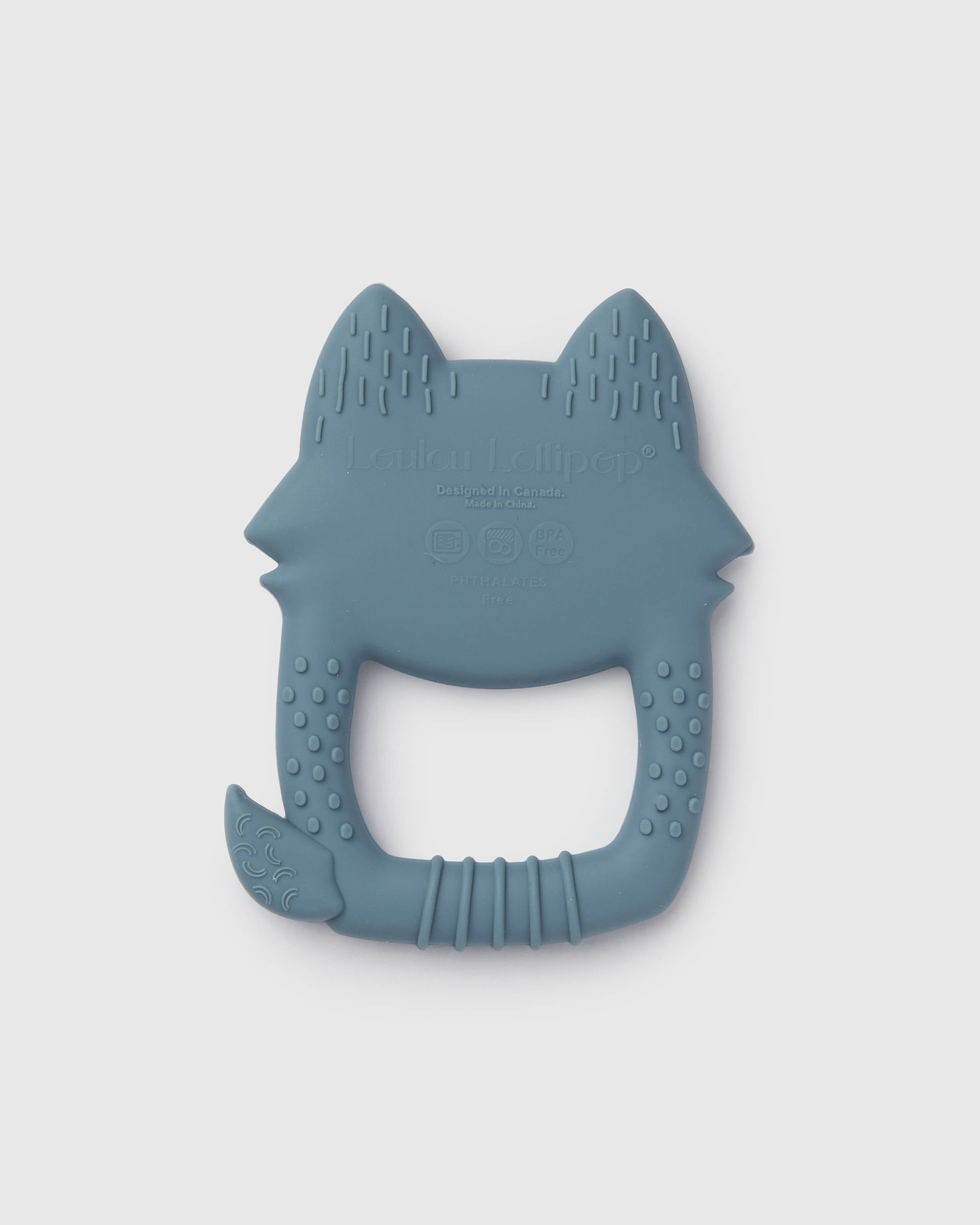 A blue-gray silicone baby teether shaped like a fox head, featuring textured ridges and a handle, shown on a light gray background.