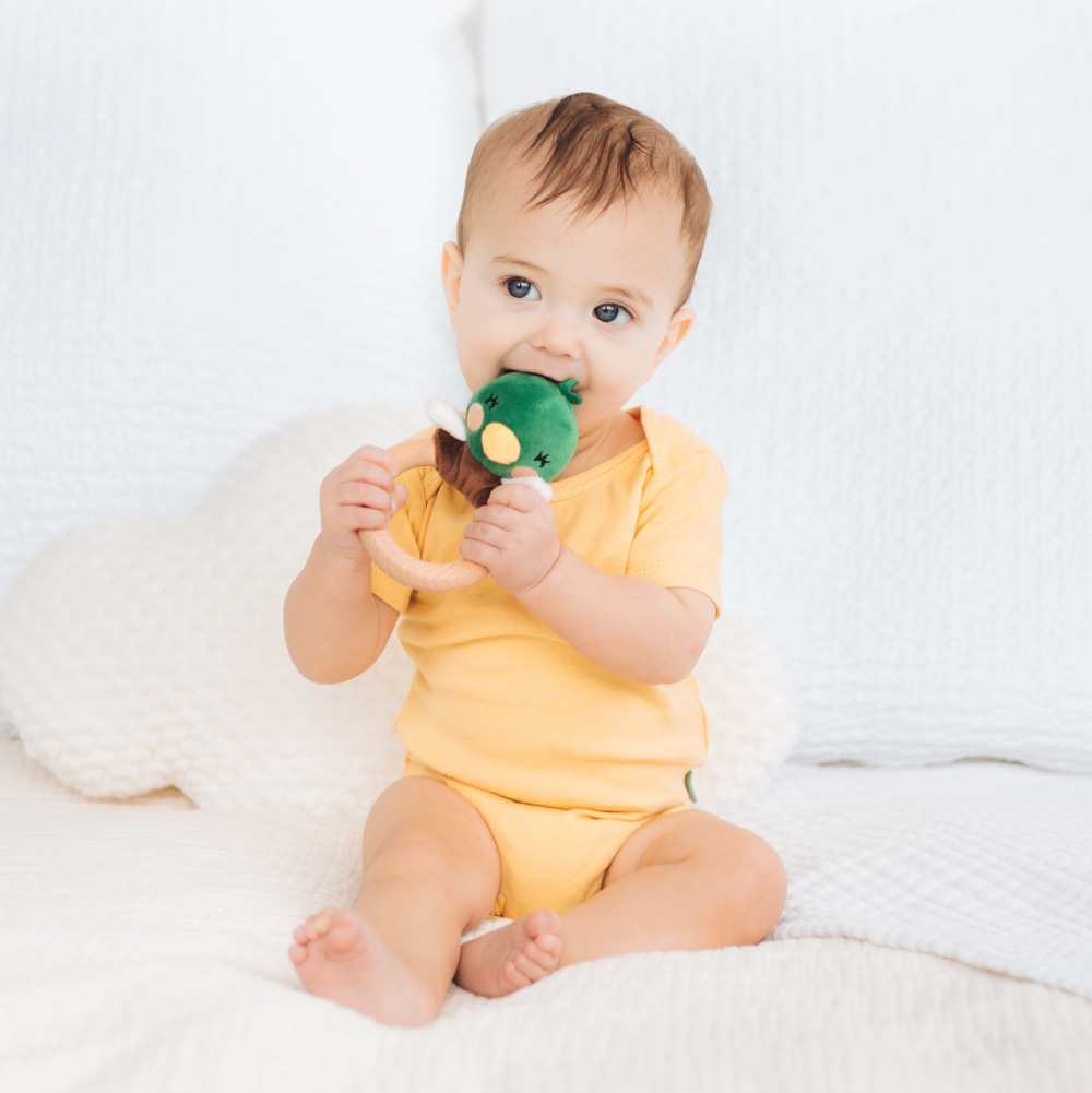 Baby in a yellow onesie holding a green toy duck on a white background