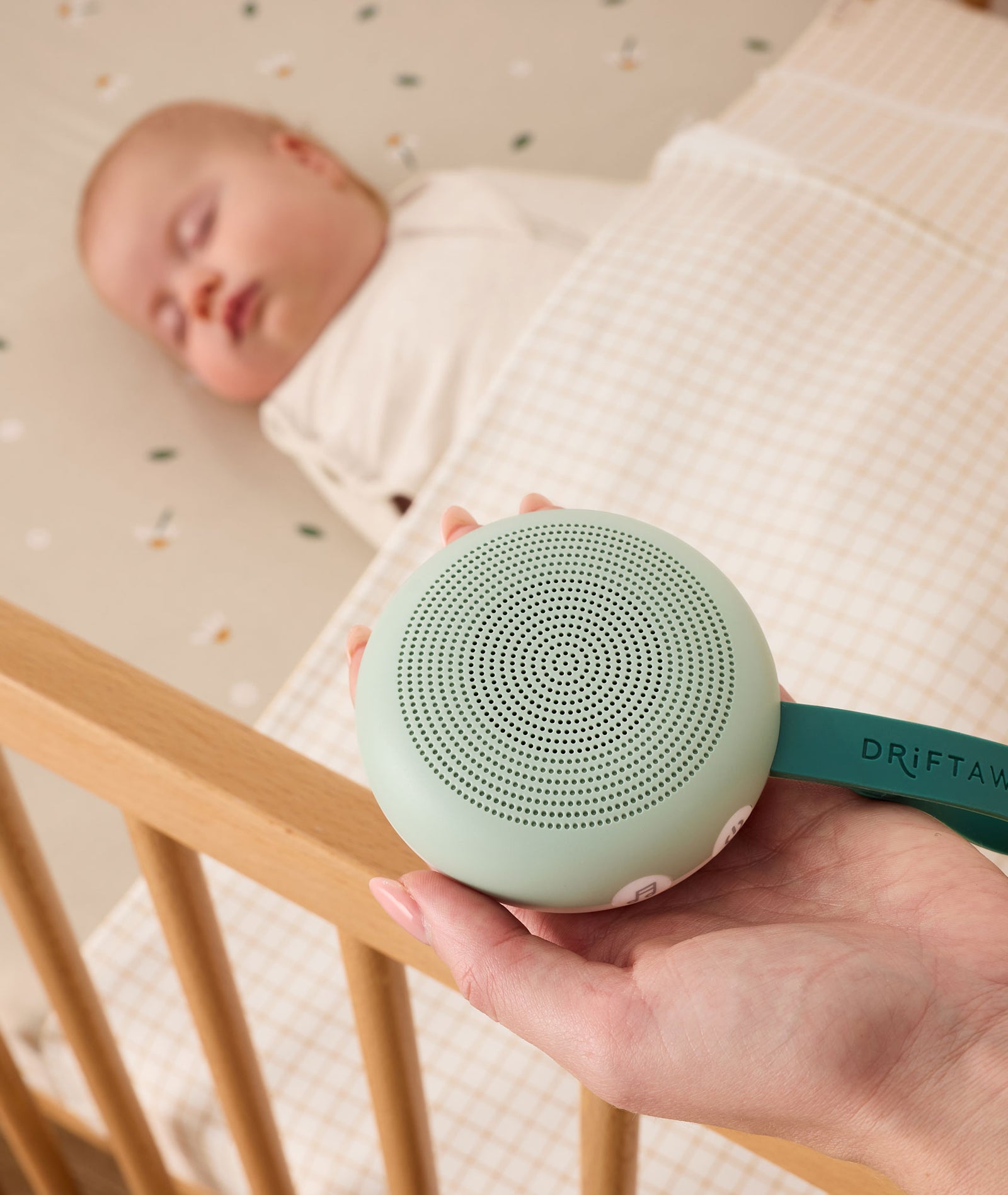 Person holding a green baby monitor device next to a sleeping baby in a crib.