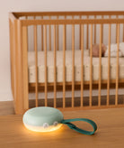 Mint green baby monitor with a glowing base on a wooden surface, with a crib and baby in the background.