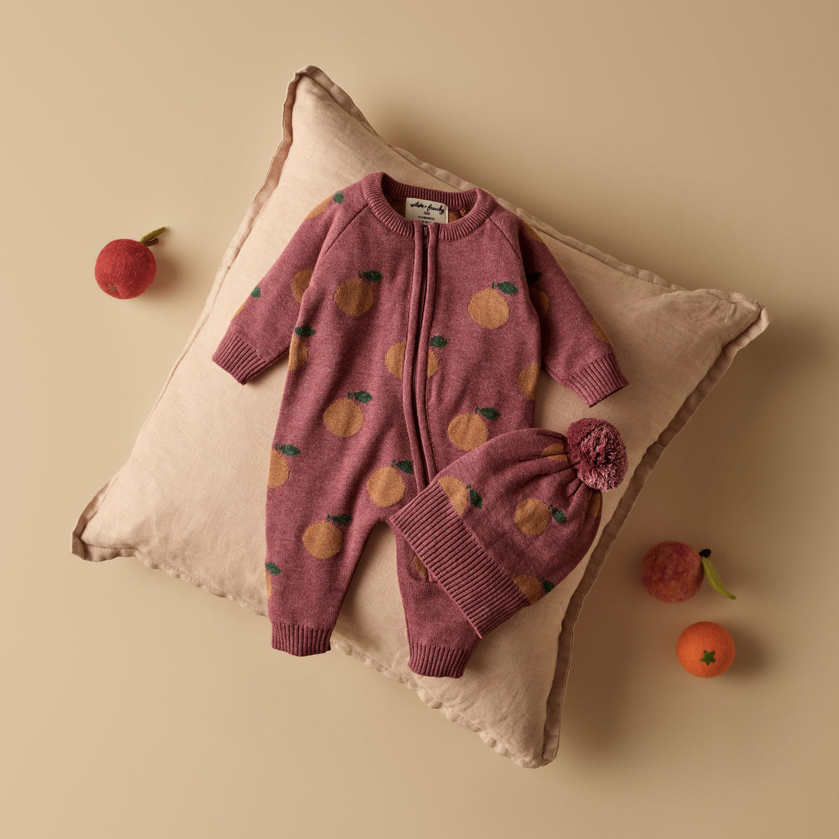 Pink baby romper with fruit pattern on a beige pillow