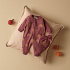 Pink baby romper with fruit pattern on a beige pillow