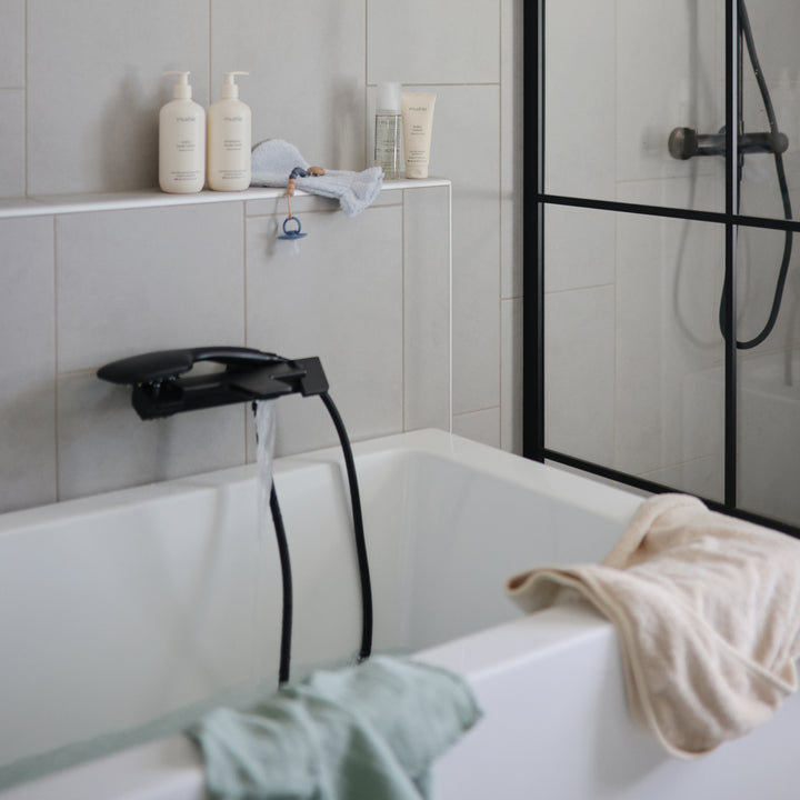 Bathroom with a bathtub, shower head, and toiletries on a shelf.