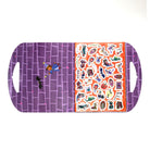 A rectangular Halloween-themed tray or board with rounded corners and side handles, shown on a white background. The left half is purple with a brick-pattern design, a small witch figure, and a black bat.