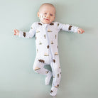 Baby wearing a white onesie with bear and tree pattern on a light green background