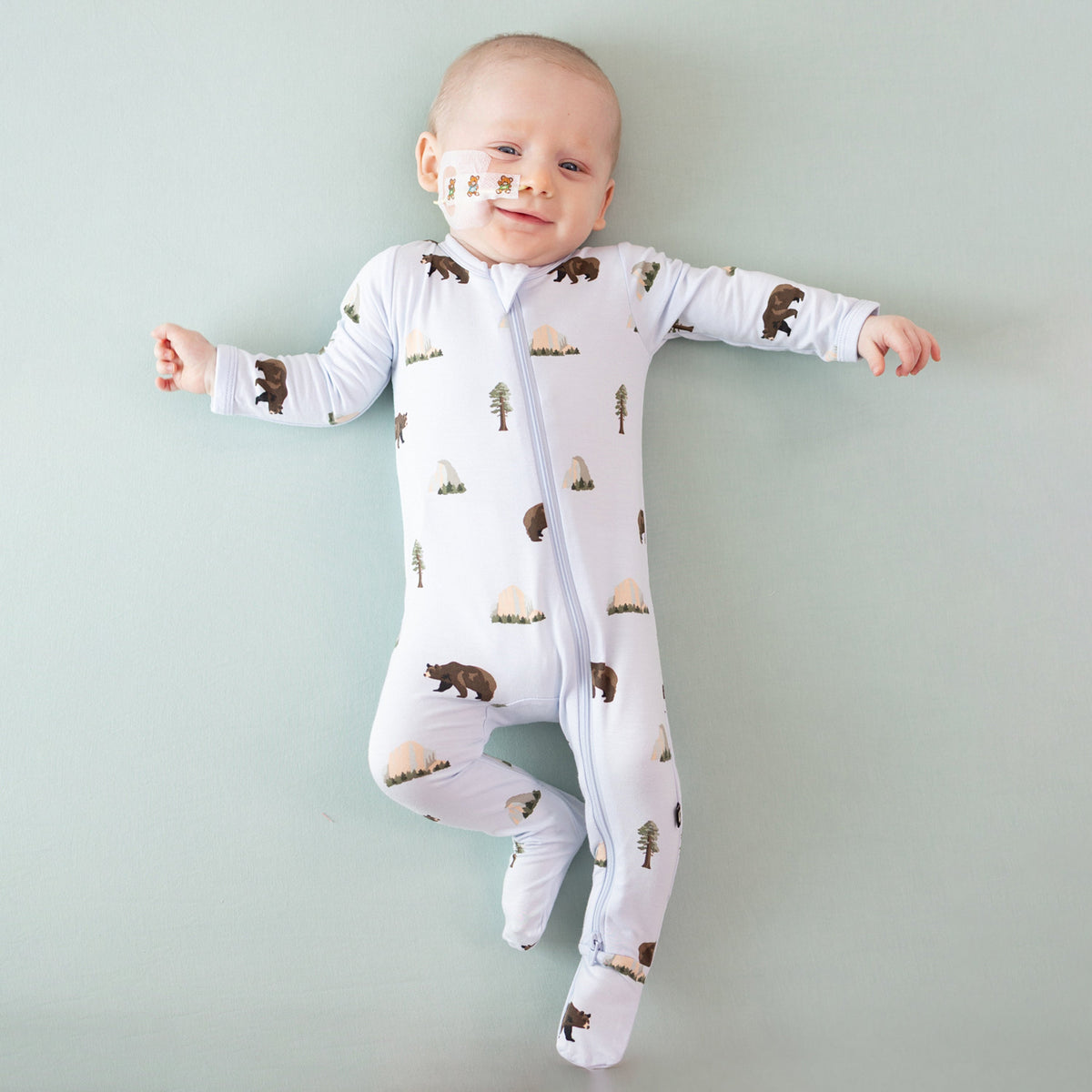 Baby wearing a white onesie with bear and tree pattern on a light green background