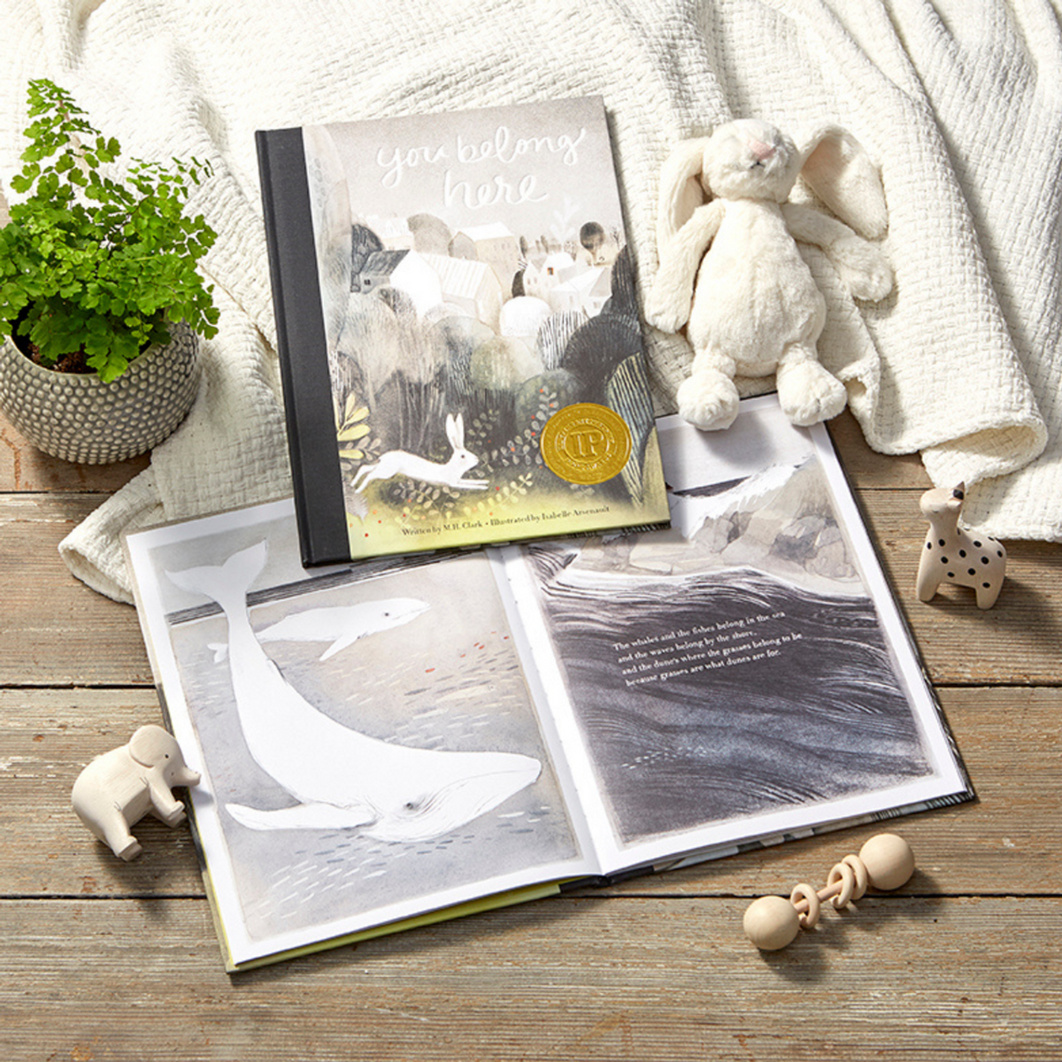 Open book with whale illustrations on a wooden surface, surrounded by toys and a plant.
