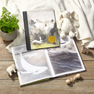Open book with whale illustrations on a wooden surface, surrounded by toys and a plant.