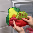 Colorful silicone vegetable-shaped container held in front of a refrigerator.