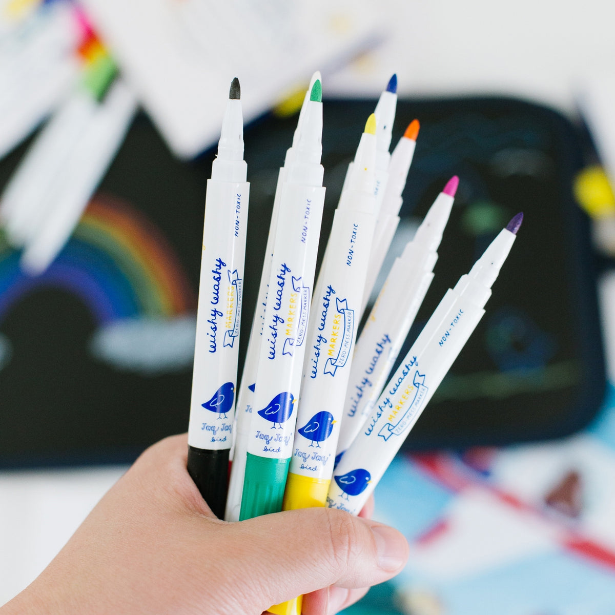 Hand holding a set of colorful markers with a blurred background