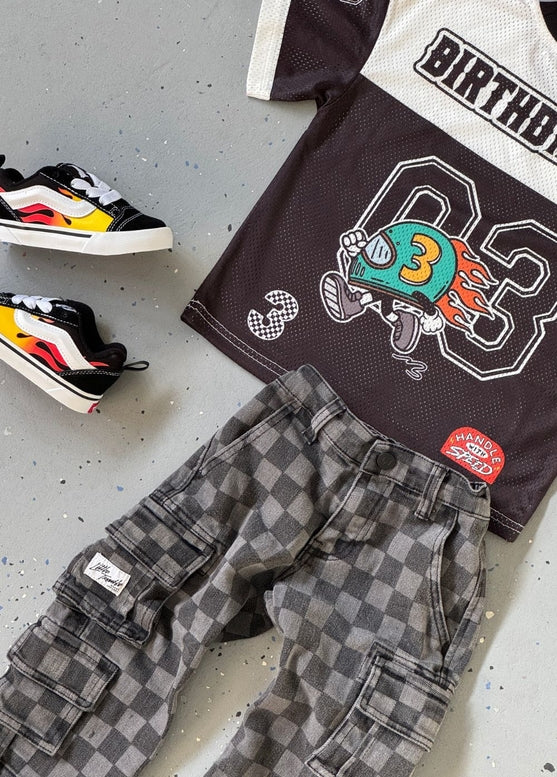 Children's t-shirt with birthday design, checkered pants, and sneakers on a gray surface
