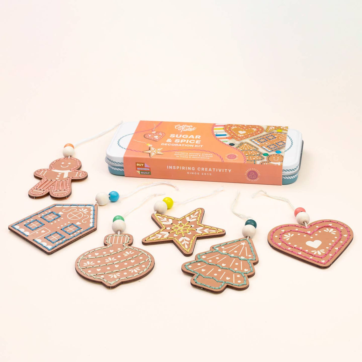 A gingerbread ornament craft kit by Sugar & Spice Workshop, featuring six decorated wooden ornaments (gingerbread man, house, ornament, star, Christmas tree, and heart) with colorful beads and strings, displayed in front of their orange and blue packaging box on a clean white background.