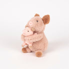 A plush stuffed animal of a pig in a soft pink coat with darker brown ears, snout, and hooves, holding a smaller pink pig toy, photographed on a seamless white background.
