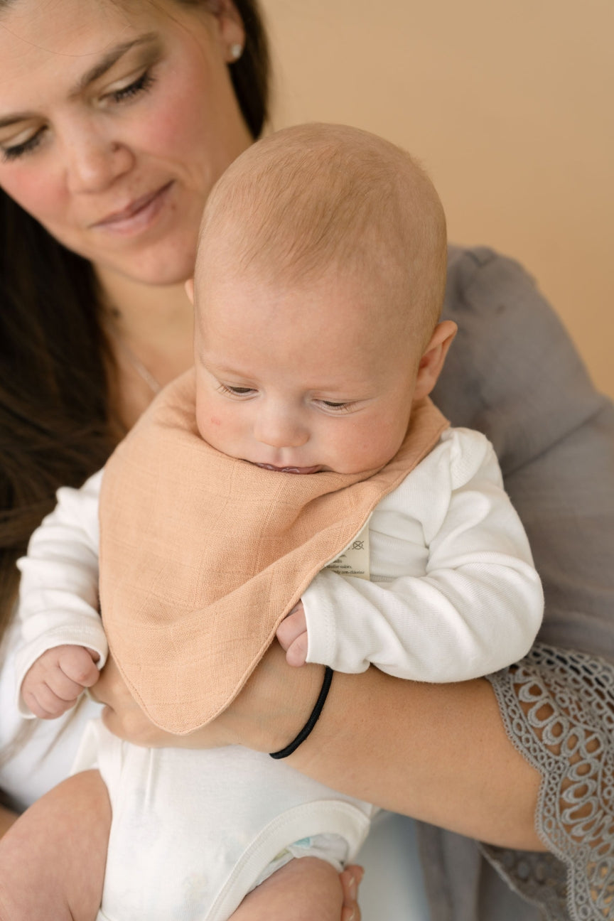 Woman holding a baby wrapped in a beige blanket against a neutral background