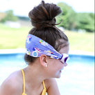 Child wearing a colorful headband and swim goggles by a pool