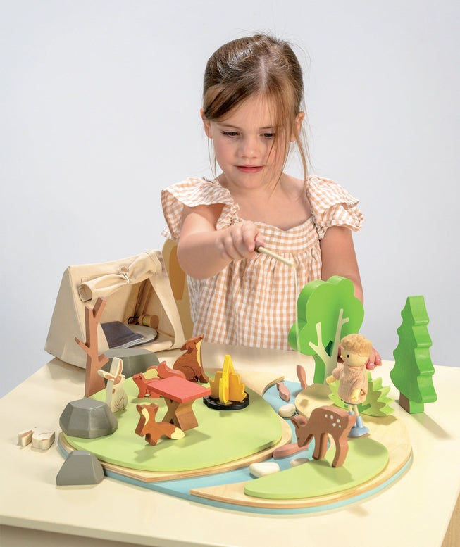 Child playing with a wooden playset featuring animals and a tent on a white background