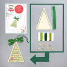 Craft kit for making a wooden Christmas tree ornament with green ribbon and decorative elements on a gray background.