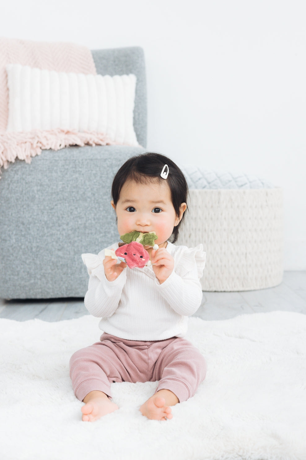 Baby sitting on a bed holding flowers with a neutral background