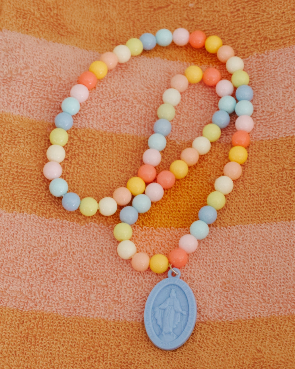 Colorful beaded bracelet with a blue pendant on an orange and pink striped fabric background