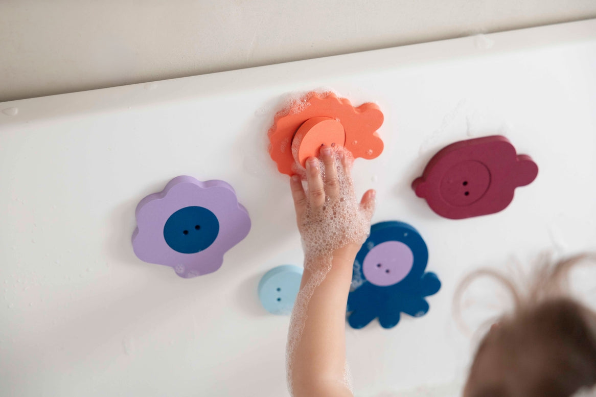 Child's hand interacting with colorful bath toys on a bathtub.