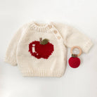 Knitted baby sweater with apple design and wooden teething ring on a light background